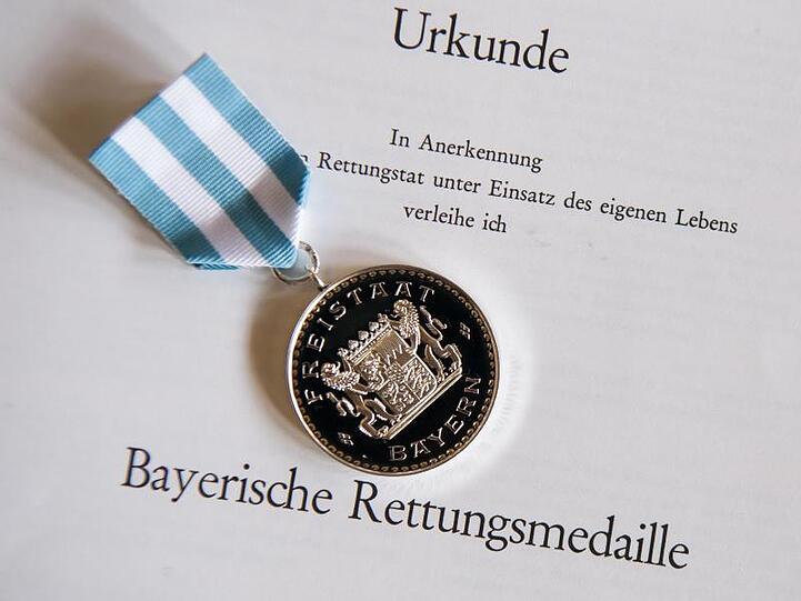 Die "Bayerische Rettungsmedaille" und die dazugehörigen Urkunde liegen während einer Verleihung zusammen. Foto: Peter Kneffel/Archivbild
