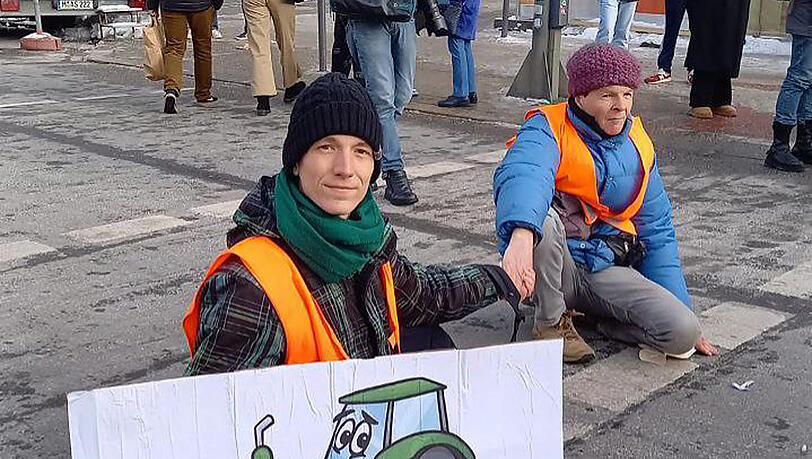 Ein Aktivist der "Letzten Generation" hält ein Plakat mit einem Traktor in der Hand.