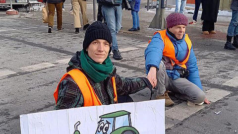 Ein Aktivist der "Letzten Generation" hält ein Plakat mit einem Traktor in der Hand.