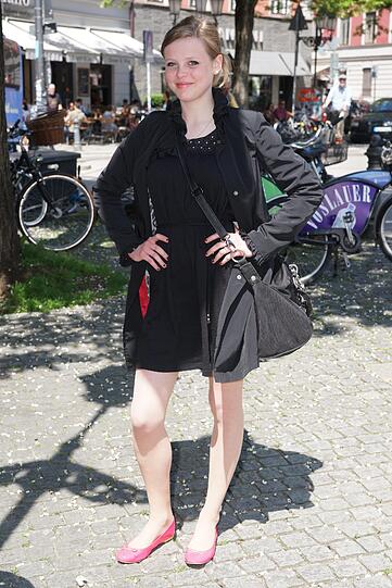 Lässig: Mantel, Kleid und Tasche in Schwarz. Dazu trägt sie rosa Ballerinas.