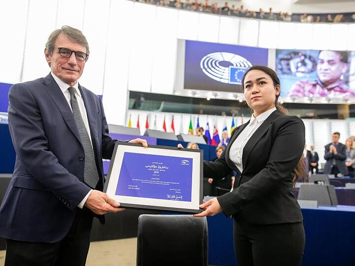 Jewher Ilham nimmt für ihren Vater den Sacharow-Preis aus den Händen des Präsidenten des Europäischen Parlaments, David Sassoli, entgegen. Im Hintergrund ist ein Foto von Ilham Tohti zu sehen.