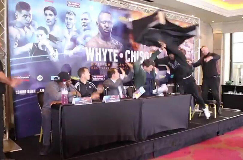 Der Video-Screenshot zeigt den Moment, in dem Chisora (r.) den Tisch auf seinen kommenden Gegner wirft.