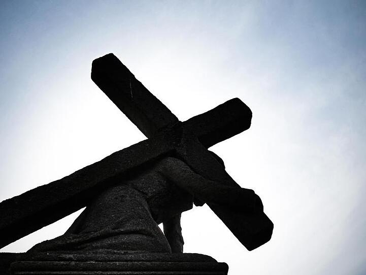 Unter blauem Himmel und gegen die Sonne zeichnet sich eine Jesusstatue unter dem Kreuz ab. Foto: Nicolas Armer/dpa/Symbolbild