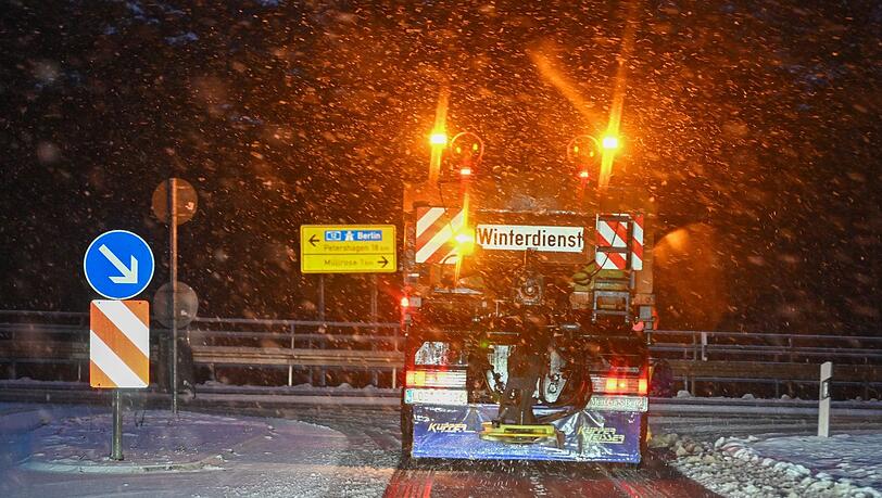 Ein Fahrzeug der Straßenmeisterei fährt im dichten Schneefall über eine Straße und streut Salz.