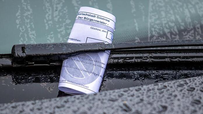 Ein Knöllchen steckt bei Regen unter dem Auto-Scheibenwischer.