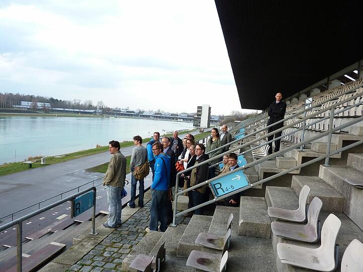 Blick vom Ende der Tribüne der Olympia-Regattaanlage auf die Bootshallen im Hintergrund. Bei der Besichtigung zum Ideenwettbewerb.
