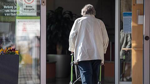 Eine Seniorin betritt mit ihrer Gehhilfe den Eingang eines Senioren-Wohnstifts.