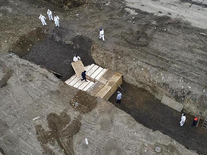 Arbeiter in Schutzanzügen vergraben schlichte Holzsärge in einem Graben auf Hart Island in der Bronx.