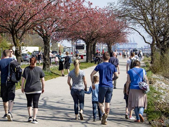 Osterausflügler gehen bei strahlendem Sonnenschein an der Elbe entlang.