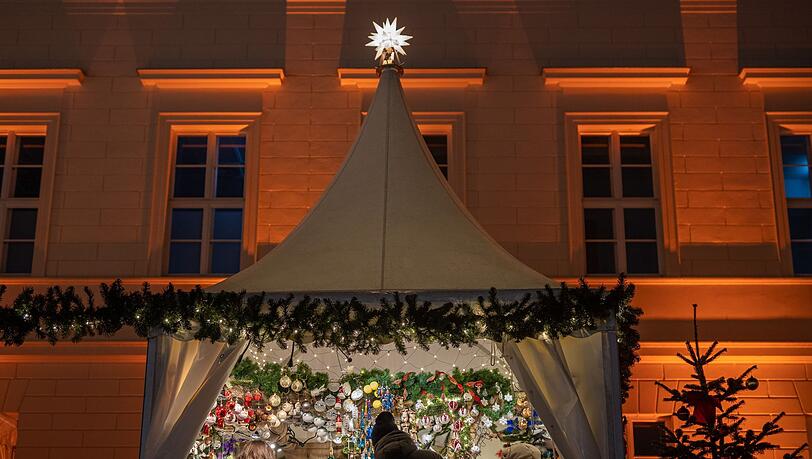 Besucher eines Weihnachtsmarktes stehen an einem Verkaufsstand für Christbaumschmuck.