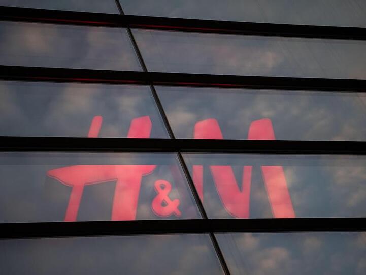Das Logo des Textilhandelsunternehmens H&M (Hennes & Mauritz) ist hinter einer Scheibe zu sehen. Foto: Marijan Murat/dpa/Archivbild