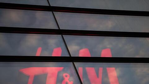 Das Logo des Textilhandelsunternehmens H&M (Hennes & Mauritz) ist hinter einer Scheibe zu sehen. Foto: Marijan Murat/dpa/Archivbild