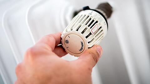 Ein Mann dreht in einer Wohnung am Thermostat einer Heizung.
