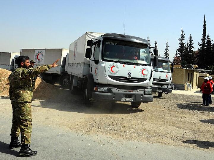 Ein syrischer Soldat weist Lastwagen des Syrisch-Arabischen Roten Halbmondes mit Hilfsgütern in Richtung eines umkämpften Gebiets (Archiv).