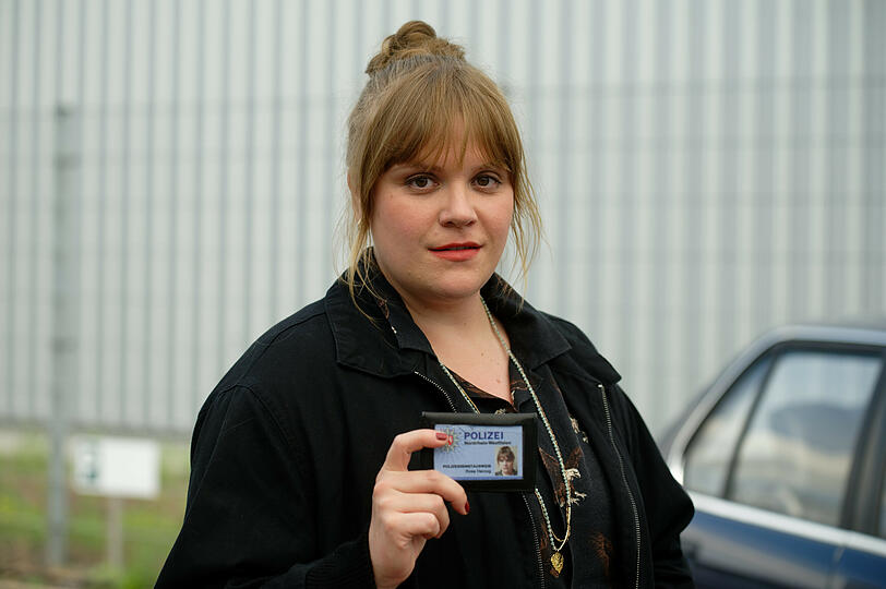 Die Schauspielerin Stefanie Reinsperger als Hauptkommissarin Rosa Herzog steht bei einem Fototermin bei Dreharbeiten zum Dortmunder "Tatort - Heile Welt" auf einem Parkplatz und zeigt ihren Dienstausweis.