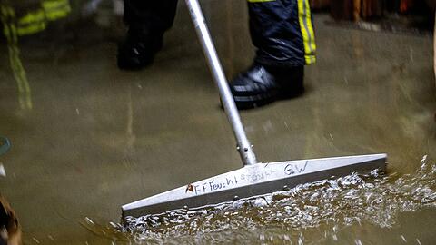 Feuerwehrleute kehren das Wasser in einem Keller zusammen und saugen es ab.