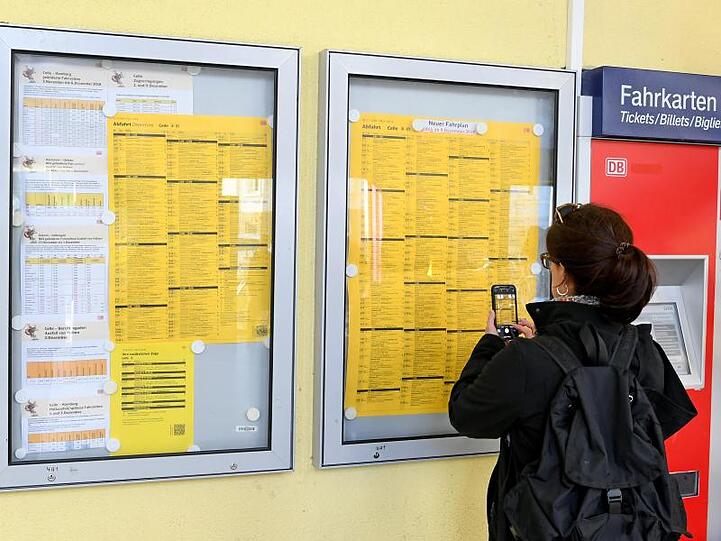 Neue Fahrpläne, gültig ab dem 09. Dezember, hängen im Bahnhof und werden von einer Frau abfotografiert. Foto: Holger Hollemann