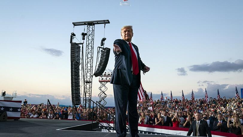 USA, Sanford: Donald Trump, Präsident der USA, wirft Gesichtsmasken in die Menge, als er zu einer Wahlkampfkundgebung am Orlando Sanford International Airport eintrifft.