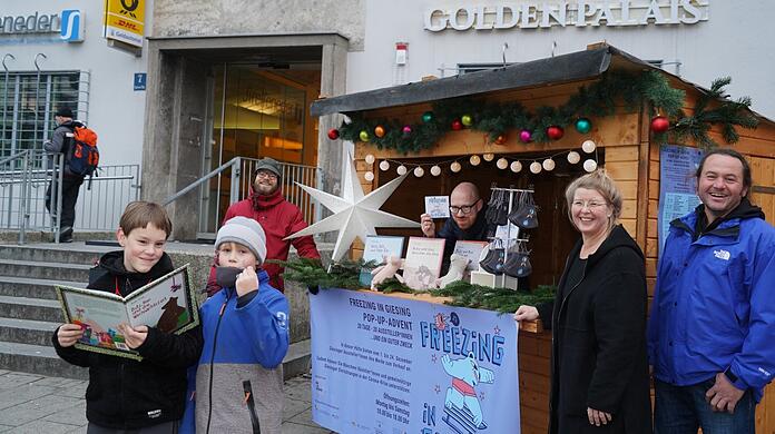 Die Brüder Elias (12) und Florian (8) stehen mit ihren Eltern Ruth Feile (Zweite Vorsitzende von "Wir in Giesing") und Robert Ployer vor Giesings neuem Pop-up-Adventsmarkt. Im Verkaufsstandl zeigt Johannes Boos, was der Verein am 1. Dezember an der Tela-Post verkaufen wird. Links neben Boos steht Vereinsmitglied Torsten Müller vom Stadteilladen Giesing.