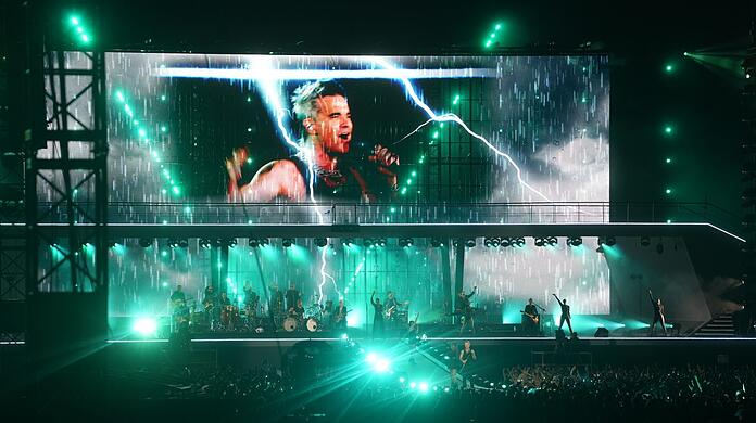Begeisterte Fans jubeln Robbie Williams auf dem Messegelände Riem zu. Und Williams nutzt die Bühne bis zum letzten Zentimeter aus - im Gegensatz zu Helene Fischer, wie so mancher sagt.