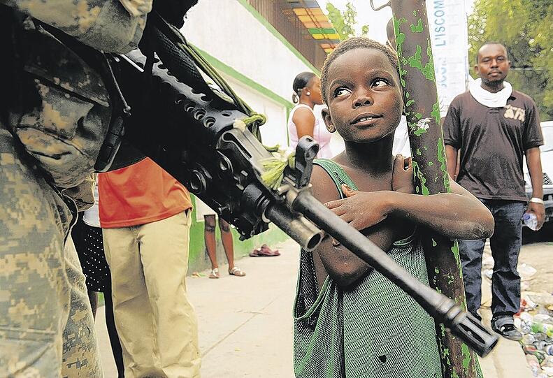 Sie tragen zwar Waffen, aber im Moment sind sie die Retter: Ein kleiner Bub schaut hoffnungsvoll zu einem Soldaten der 82. US-Luftlandedivision auf.Foto: Polaris