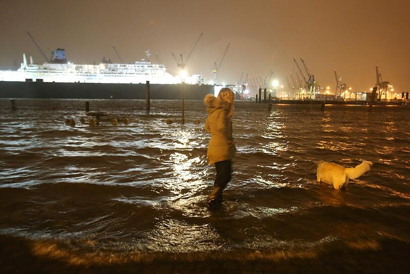 Ein Frau begibt sich während der Sturmflut in Hamburg in Lebensgefahr und geht mit ihrem Hund in der Nähe des überfluteten Fischmarkts spazieren.