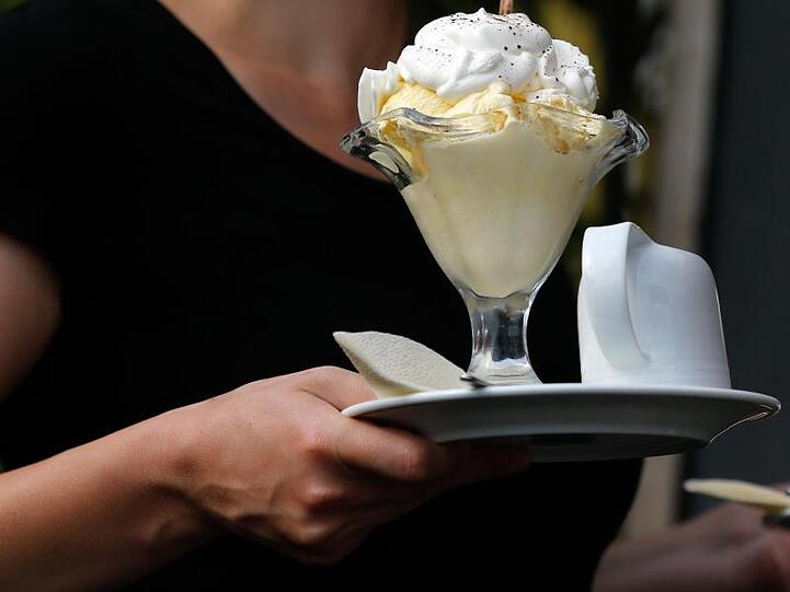 Eine Kellnerin serviert in einer Gaststätte einen Eisbecher. In Deutschland bekommen viele Beschäftigte nicht den Stundenlohn, der ihnen zusteht.