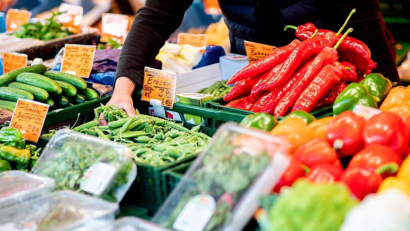 Ein Verkäufer greift an einem Obst- und Gemüsestand auf dem Wochenmarkt in eine Kiste mit Erbsen.
