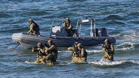 Taucher machen den Anfang und steigen aus dem Wasser auf den schneebedeckten Strand, um den K&uuml;stenabschnitt zu sichern.