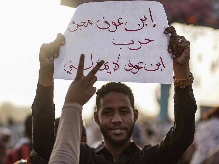 Ein Demonstrant hält ein Plakat, auf dem auf Arabisch steht: "Ibn Ouf ist ein Kriegsverbrecher, Ibn Ouf vertritt mich nicht". Viele Protestler kritisieren, dass nun der bisherige Vizepräsident Awad Ibn Auf die Macht übernommen hat.