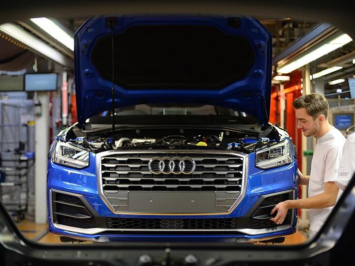 Ein Mitarbeiter bringt an einem Fließband im Audi-Werk das Frontende an einem Audi an. Foto: dpa