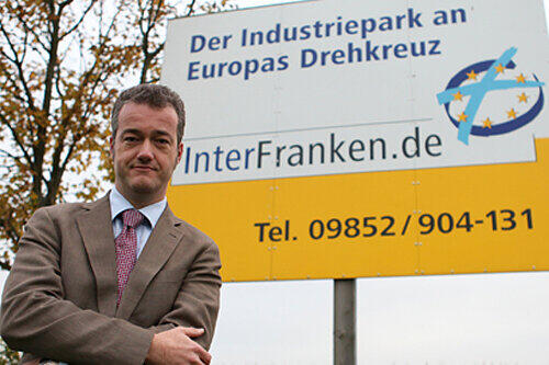 Feuchtwangens Bürgermeister Patrick Ruh vor dem Werbeschild zum Gewerbepark &bdquo;InterFranken&ldquo;.