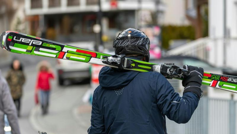 Ein Skifahrer geht mit geschulterten Skiern auf einer Straße im Skiort Ischgl.