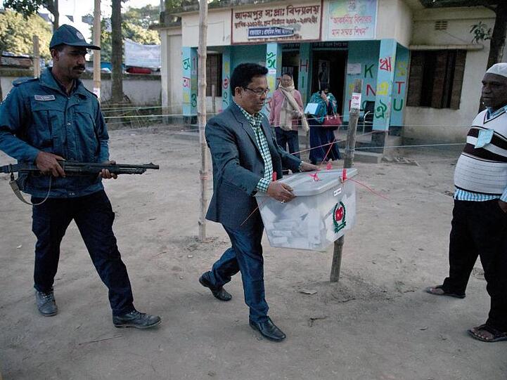 Unter Polizeischutz trägt ein Wahlhelfer nach Ende der Stimmabgabe eine Wahlurne aus einem Wahllokal in Dhaka.
