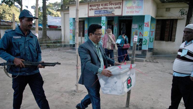 Unter Polizeischutz trägt ein Wahlhelfer nach Ende der Stimmabgabe eine Wahlurne aus einem Wahllokal in Dhaka. Unter Polizeischutz trägt ein Wahlhelfer nach Ende der Stimmabgabe eine Wahlurne aus einem Wahllokal in Dhaka.