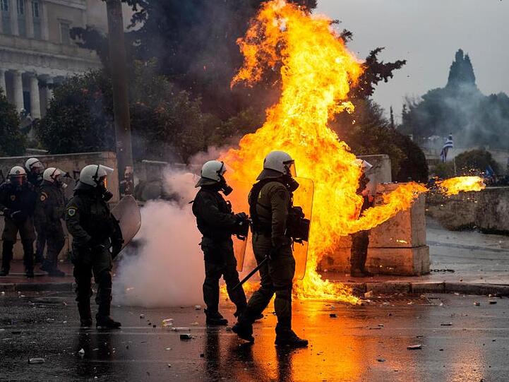 Griechische Bereitschaftspolizisten stehen vor einer Feuerwand, verursacht durch einen Molotow-Cocktail.