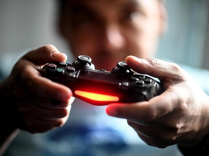 Ein junger Mann spielt mit der Spielekonsole Playstation vor dem Fernseher.