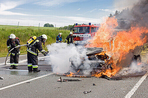 Die Feuerwehr löscht das brennende Auto, in dem sich noch zwei Personen befinden