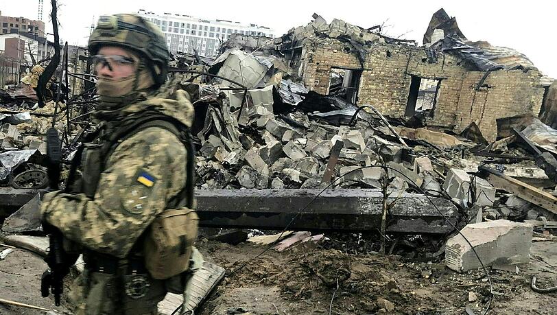 Ein ukrainischer Soldat läuft in Butscha an den Trümmern zerstörter Häusern vorbei.