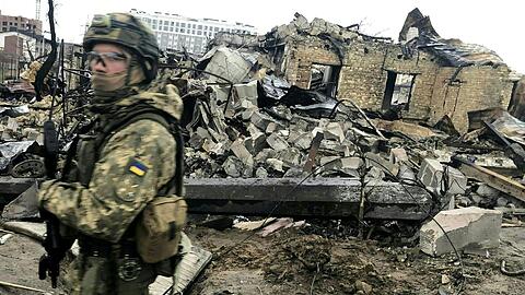 Ein ukrainischer Soldat läuft in Butscha an den Trümmern zerstörter Häusern vorbei.