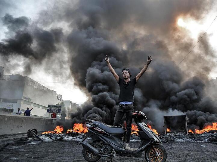 Ein Demonstrant steht in Beirut auf einem Motorroller und gestikuliert vor einer Barrikade.