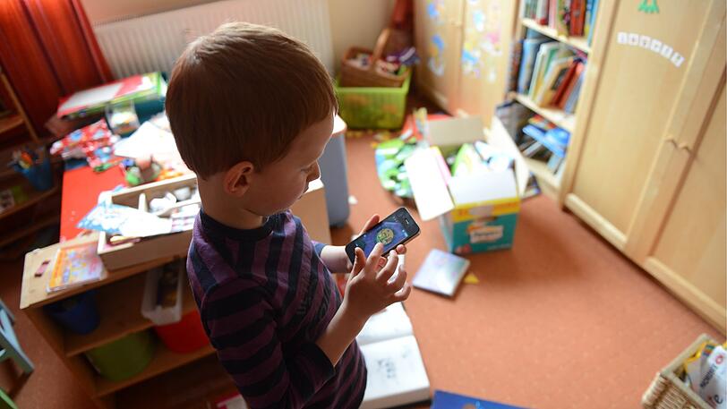 Ein kleiner Bub spielt mit einem Smartphone in seinem Kinderzimmer.