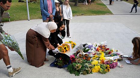 Zahlreiche Menschen legen am Tatort Blumen nieder.