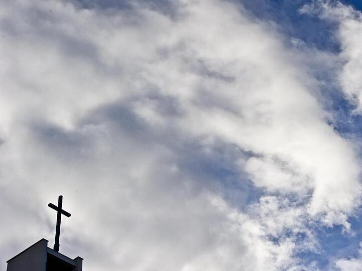 Das Kreuz einer Kirche ist vor bewölktem Himmel zu sehen. Foto: Nicolas Armer/Archiv
