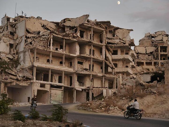 Motorradfahrer passieren zerstörte Gebäude in der Provinz Idlib. Das Auswärtige Amt schätzt nicht nur die Region um Idlib, sondern ganz Syrien als gefährlich für Rückkehrer ein.
