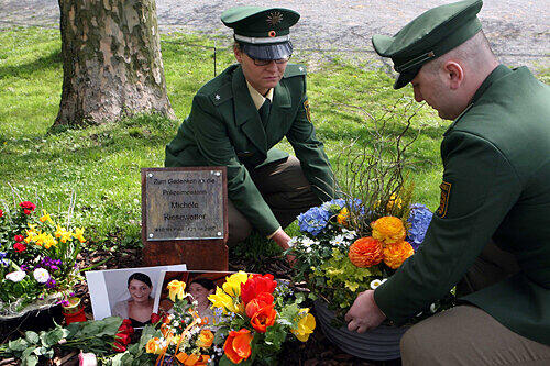 Eine Polizistin und ein Polizist stellen eine Blumenschale bei der Gedenktafel nieder, die an die ermordete Polizistin erinnert.