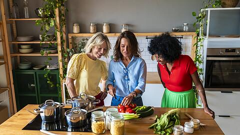 Drei Frauen kochen mit frischen Zutaten. Eine dauerhafte Umstellung des Essverhaltens führt langfristig ans Ziel.