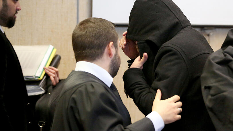Ein Angeklagter steht mit Kapuze über dem Gesicht im Landgericht Köln zwischen seinen Anwälten.