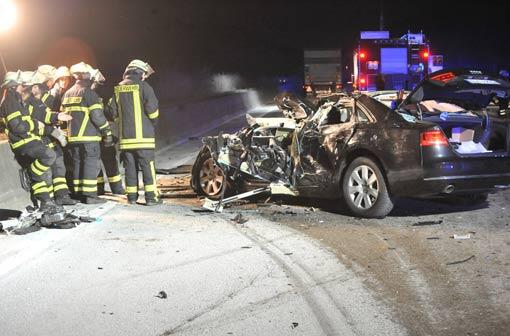 Helfer stehen auf der Autobahn A 1 vor einem völlig demolierten Wrack eines Audis.