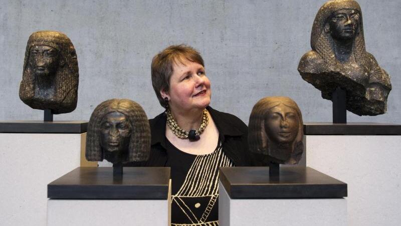 Sylvia Schoske steht zwischen vier Portraitköpfen.